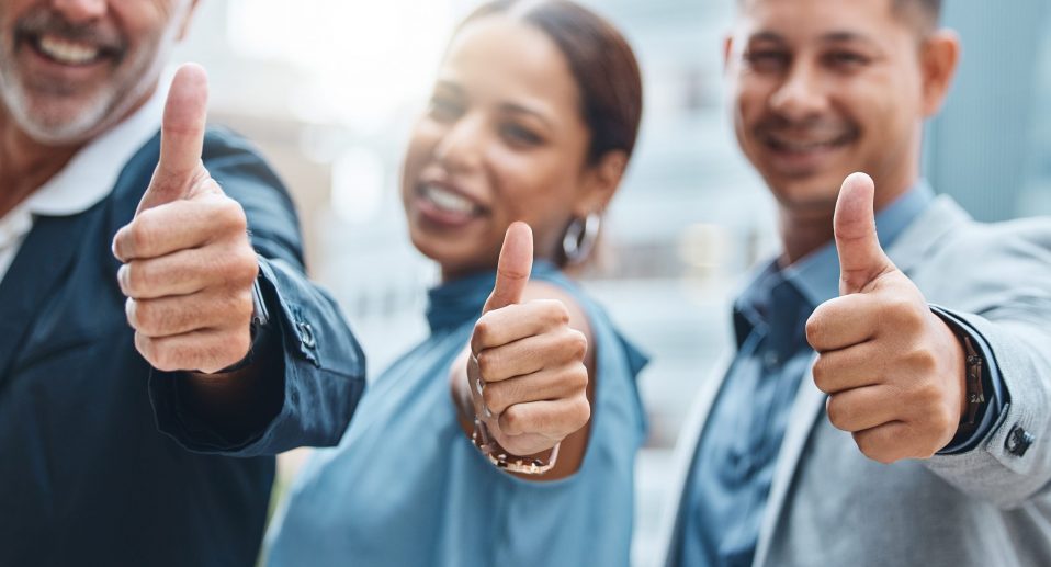 Shot of a group of businesspeople showing thumbs up against an urban background.